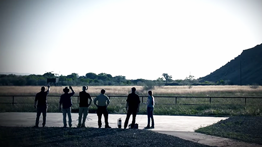 Six silhouetted figures look into the sky over rural farmland