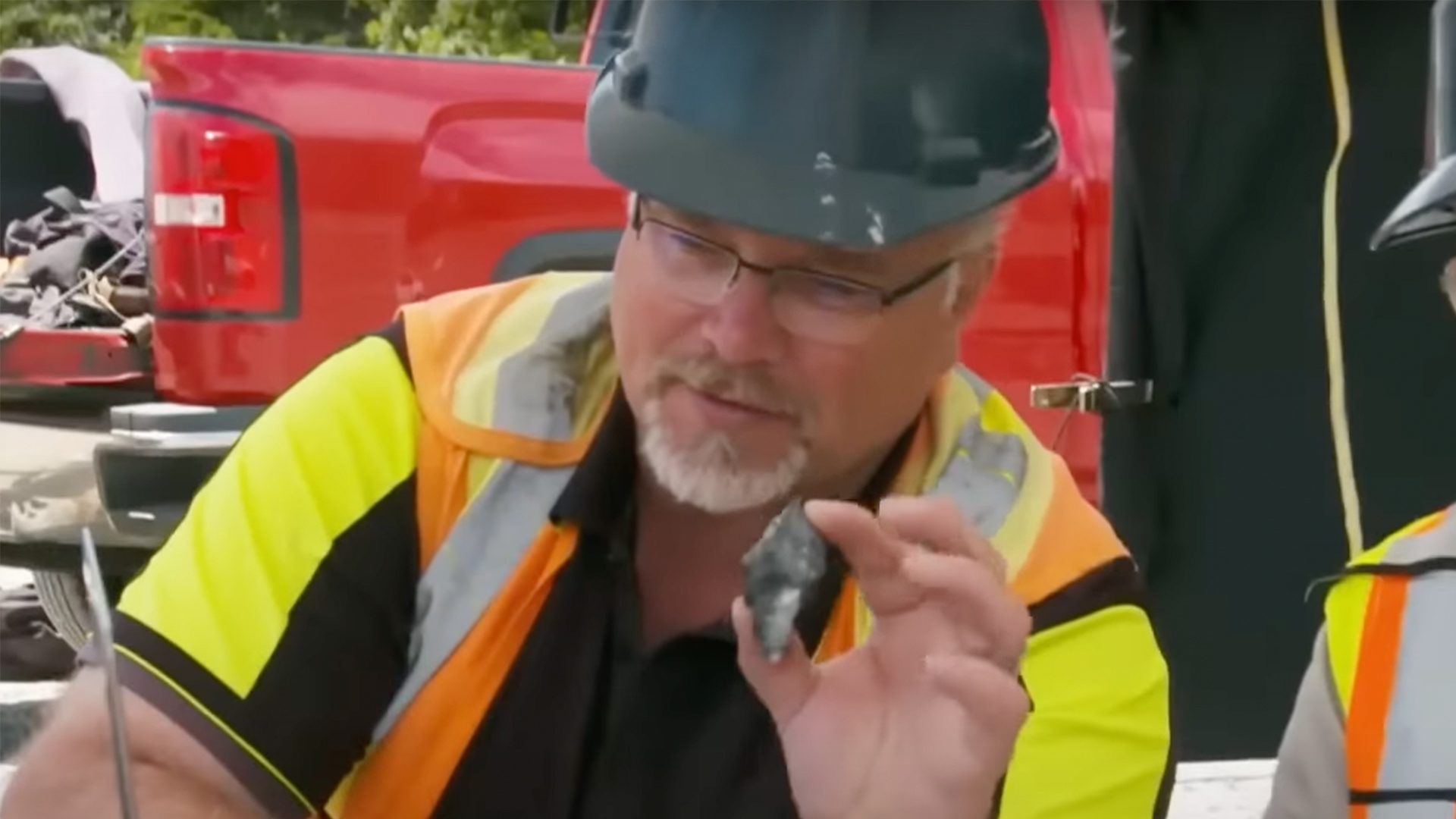 A man in a high vis jacket and hard hat holds up an interesting rock