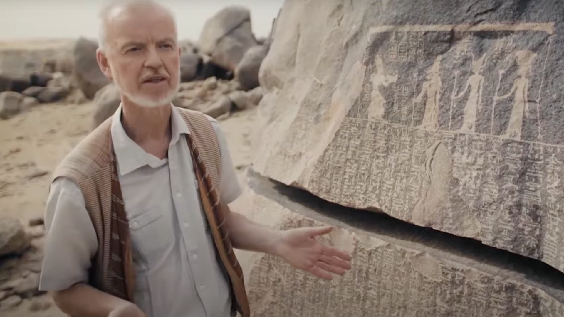 An Egyptologist talking next to some hieroglyphics on a rock