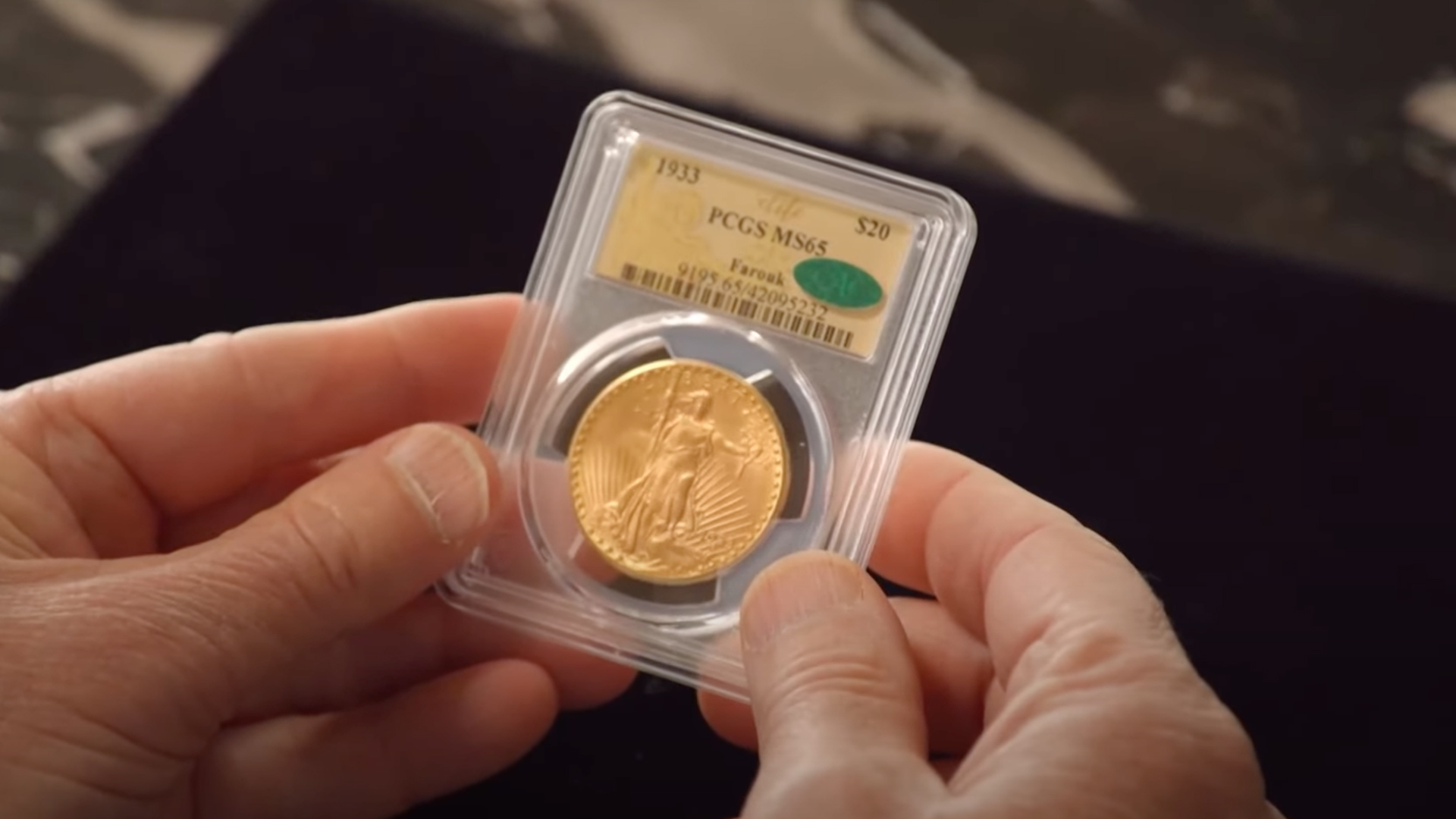 A shiny gold coin in a protective case being held in a man's hands