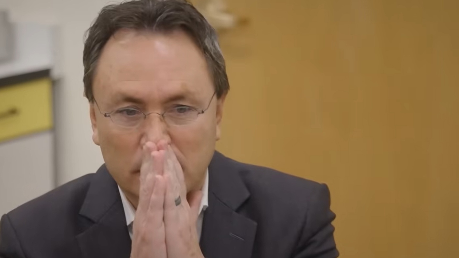 Brandon Frugal looking pensive, holding his hands in front of his mouth in a prayer-like pose.