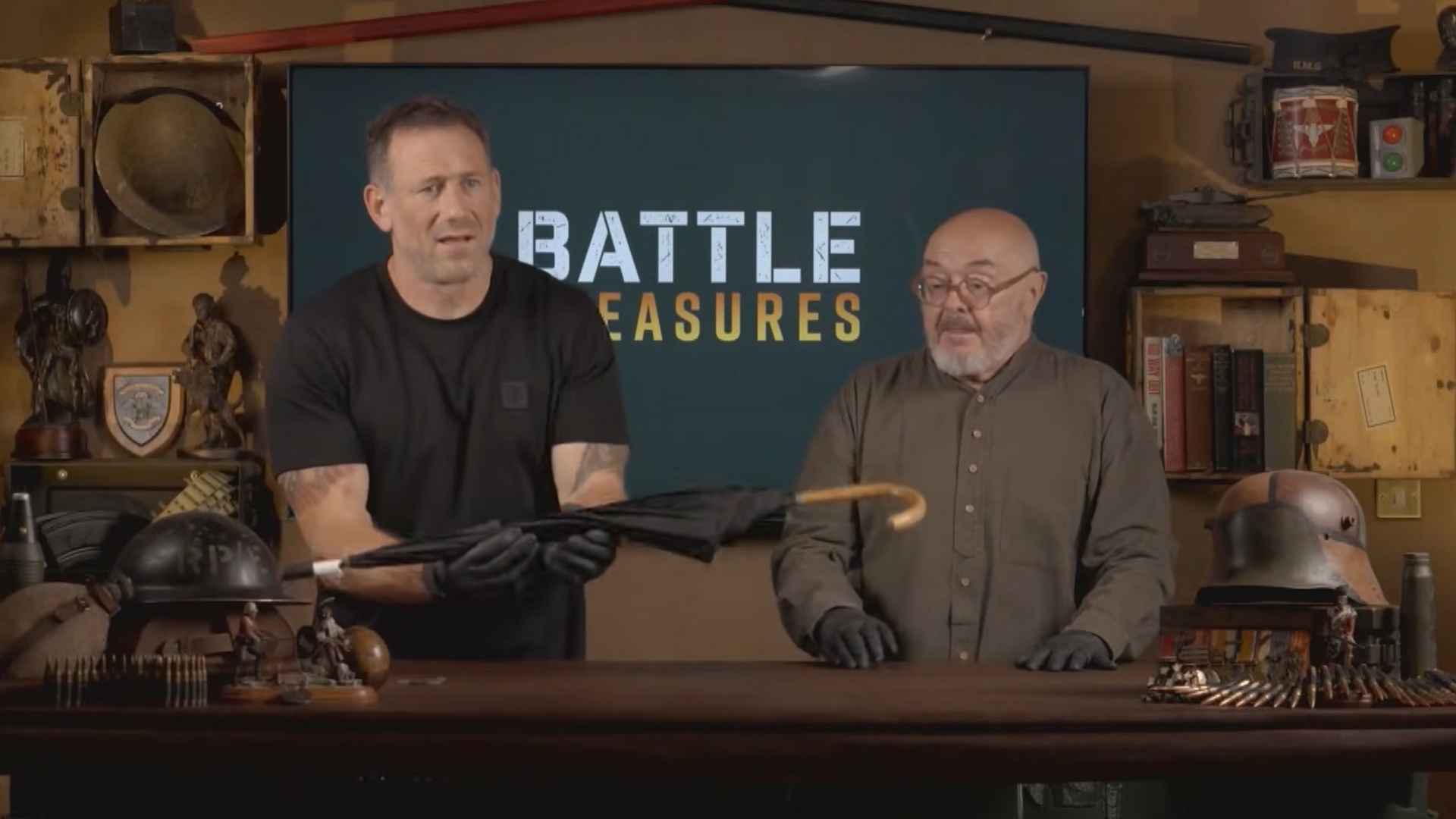 Bruce Crompton watches on as Jason Fox carefully holds a black umbrella 