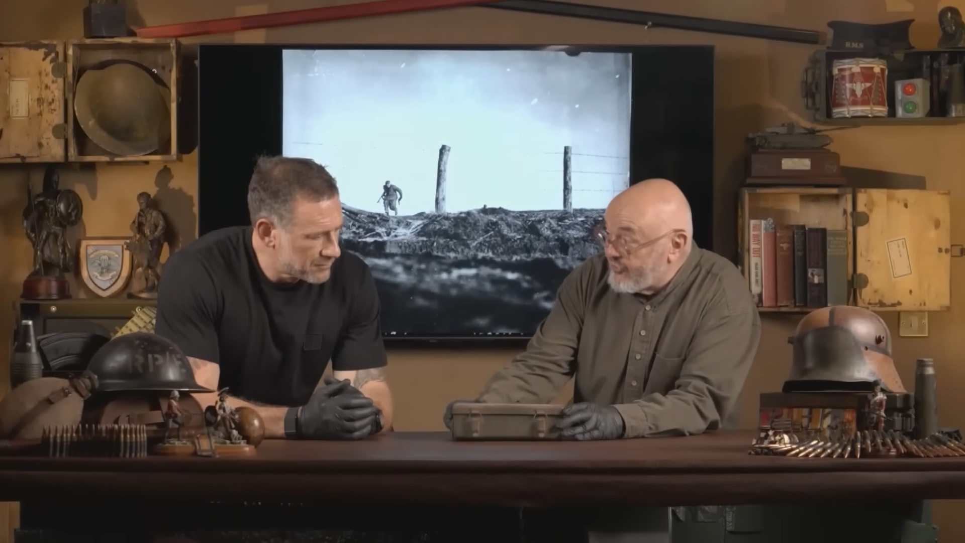 Foxy and Bruce inspecting an old container in front of an image from WWII