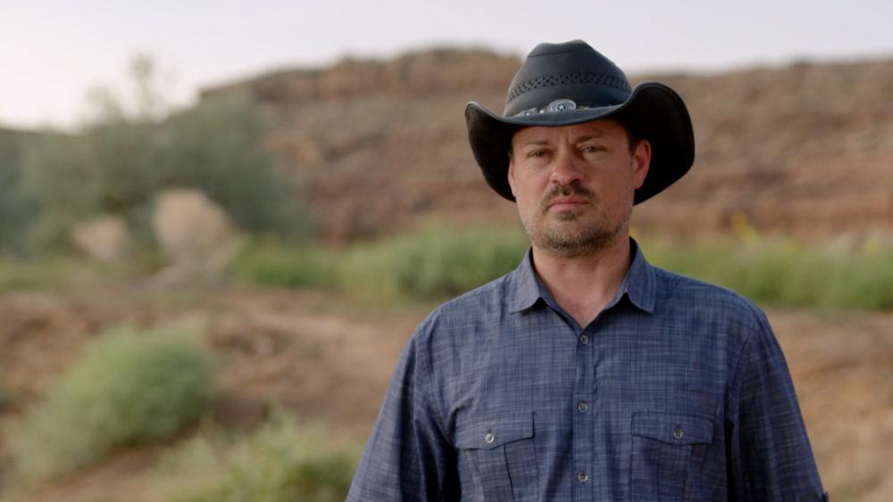 Thomas Winterton is wearing a cowboy hat while standing in the desert and is about to talk to the camera
