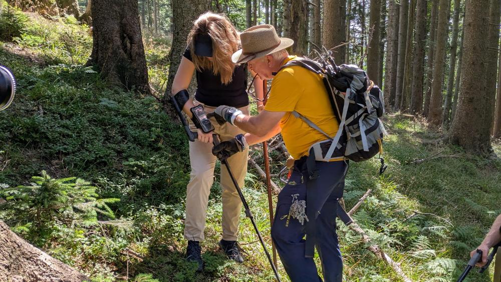 Jurgen Proske helps Justine Ostrowska with a metal detector in a mountainside forest