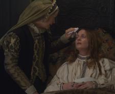 An actor portraying Queen Mary has her forehead dabbed while she's ill in bed