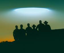 Silhouette of the Curse of Skinwalker Ranch team against a hazy evening sky with lights from a UFO hovering above them