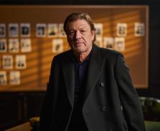 Sean Bean sitting in front of an evidence board