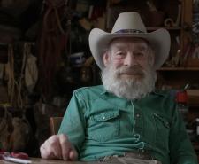 Tom Oar sitting in his home wearing a green shirt and a cowboy hat