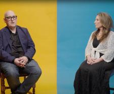 A man and a woman sitting either side of a divided background which is yellow on the left and blue on the right
