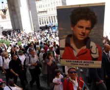 A woman in a crowd holds a sign of Carlo Acutis' face during his canonisation in Vatican City