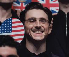 Timothée Chalamet in 'Marty Supreme' smiles while holding a ping pong paddle with the US flag on it