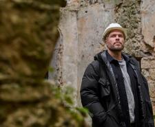 Rick Edwards wearing a white hard hat walking through the ruins of an old castle