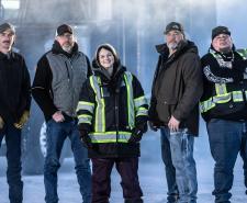The Ice Road Truckers cast standing in front of a large truck in icy conditions