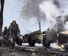Colourised image of German soldiers passing burning U.S. equipment in the beginning of the Battle of the Bulge