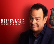 Dan Aykroyd next to the show title with a one-legged pigeon standing on his shoulder. The pigeon is wearing a WWI helmet and has a military medal around its neck