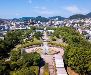 High angle view of Nagasaki Peace Park in Japan. Scenery consist of statues, many buildings, blue sky with cloud and green trees.