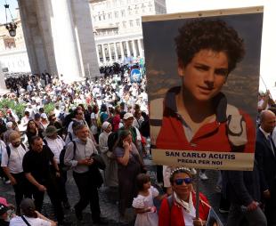 A woman in a crowd holds a sign of Carlo Acutis' face during his canonisation in Vatican City