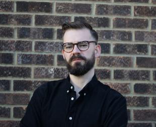 Dr Daniel Cowling standing in front of a brick wall