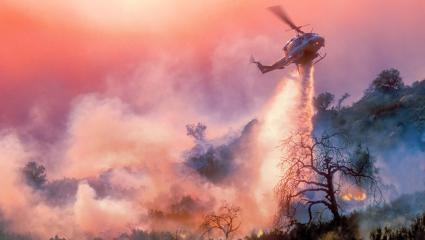 A helicopter dropping water on a wildfire in California