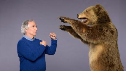 Henry Winkler holding up his fists while facing a stuffed brown bear