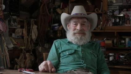Tom Oar sitting in his home wearing a green shirt and a cowboy hat