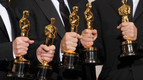 Five men in suits holding Oscar statues