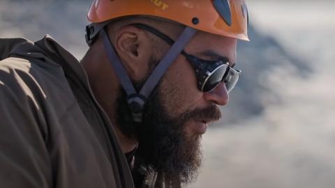 An explorer wearing a hard hat and sunglasses on the side of a snowy mountain