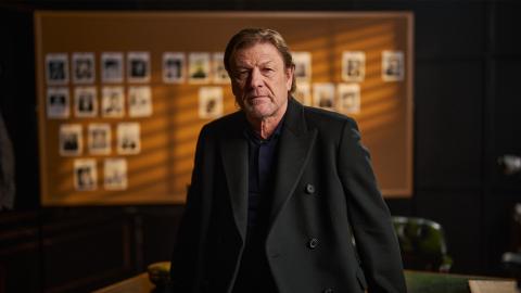 Sean Bean sitting in front of an evidence board