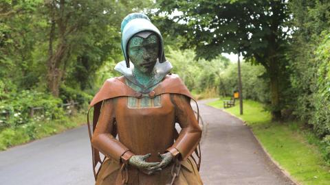 A copper statue depicting a woman in chains dressed in 16th/17th century clothes
