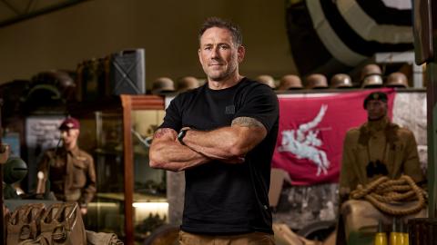 Jason Fox standing with his arms crossed in front of a lot of military artefacts