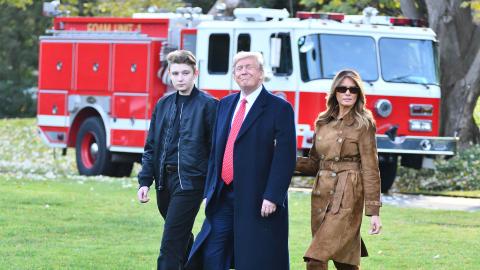 Donald Trump with his wife and son walking across grass with a fire truck in the background