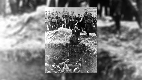 A Nazi solider points a gun at a Jewish man's head as he kneels over a mass grave