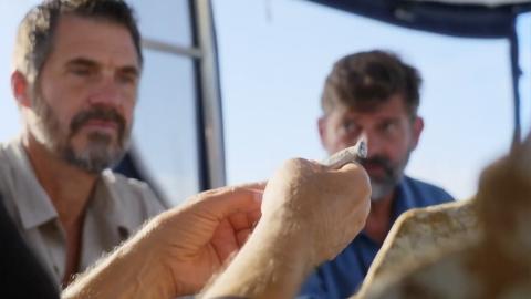 Men inspect a small silver pipe they found on the seabed