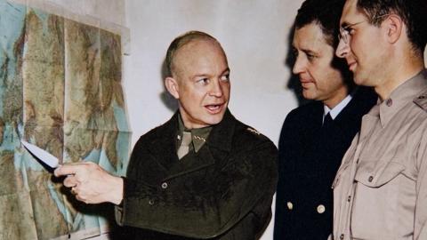 General Dwight Eisenhower points to a map during Operation Torch planning in World War II as military staff look on.