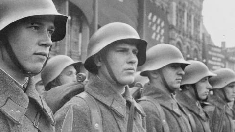 Black-and-white photo of uniformed soldiers in steel helmets and heavy coats standing in formation on a city street.
