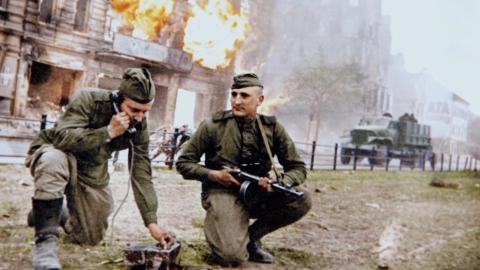 Two soldiers in front of an exploding building in WWII