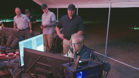Travis Taylor looks at a monitor during an outside, nighttime experiment while other members of the team look on