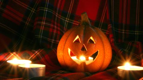 A pumpkin on Scottish tartan next to some candles