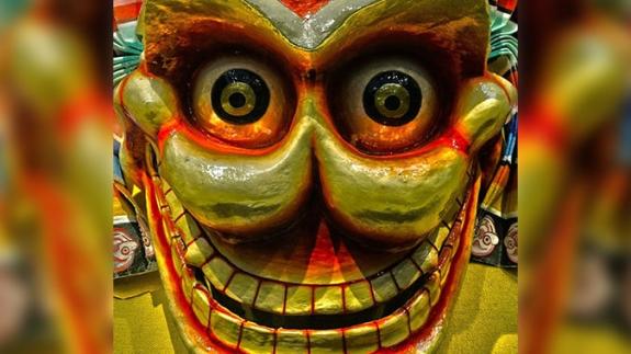 A gold and red Tibetan Skull mask, depicting a smiling face