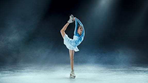 A female figure skater performs and acrobatic move in a blue dress