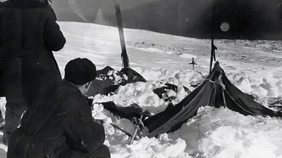 A man crouches next to a destroyed tent on the side of a snowy mountain