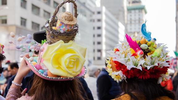 Two women wearing extravagant hats adorned with colourful flowers and eggs