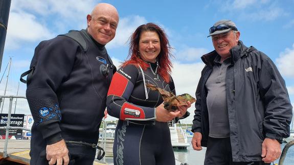 Ross Kemp, Mallory Haas and Neil Brock posing with a piece of copper hull sheath
