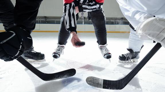 Hockey referee with puck standing on ice rink with two rivals with sticks on his right and left waiting for moment to shoot it