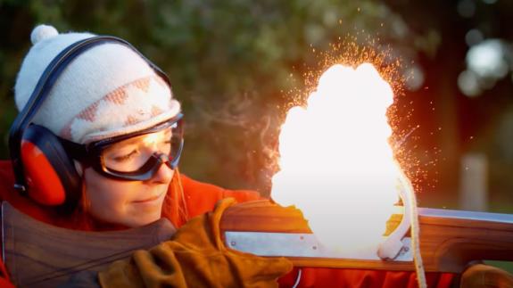 A small explosion of gunpowder emits from a gun fired by Alice Roberts