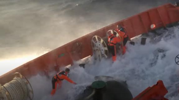 A wave comes over the side of a large boat, soaking the workers on board