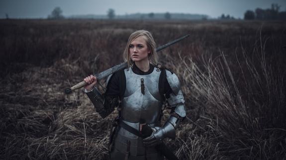A woman holding a sword and wearing armour standing in a field