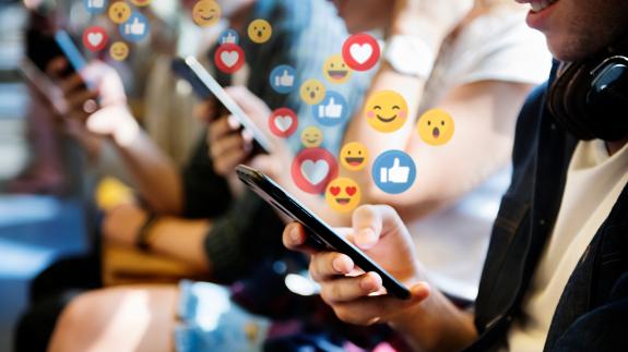 An edited photograph of a person holding a phone with emojis floating from the screen