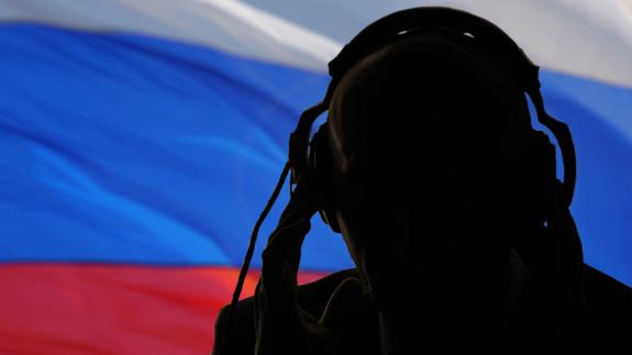 A man wearing headphones in front of the Flag of Russia